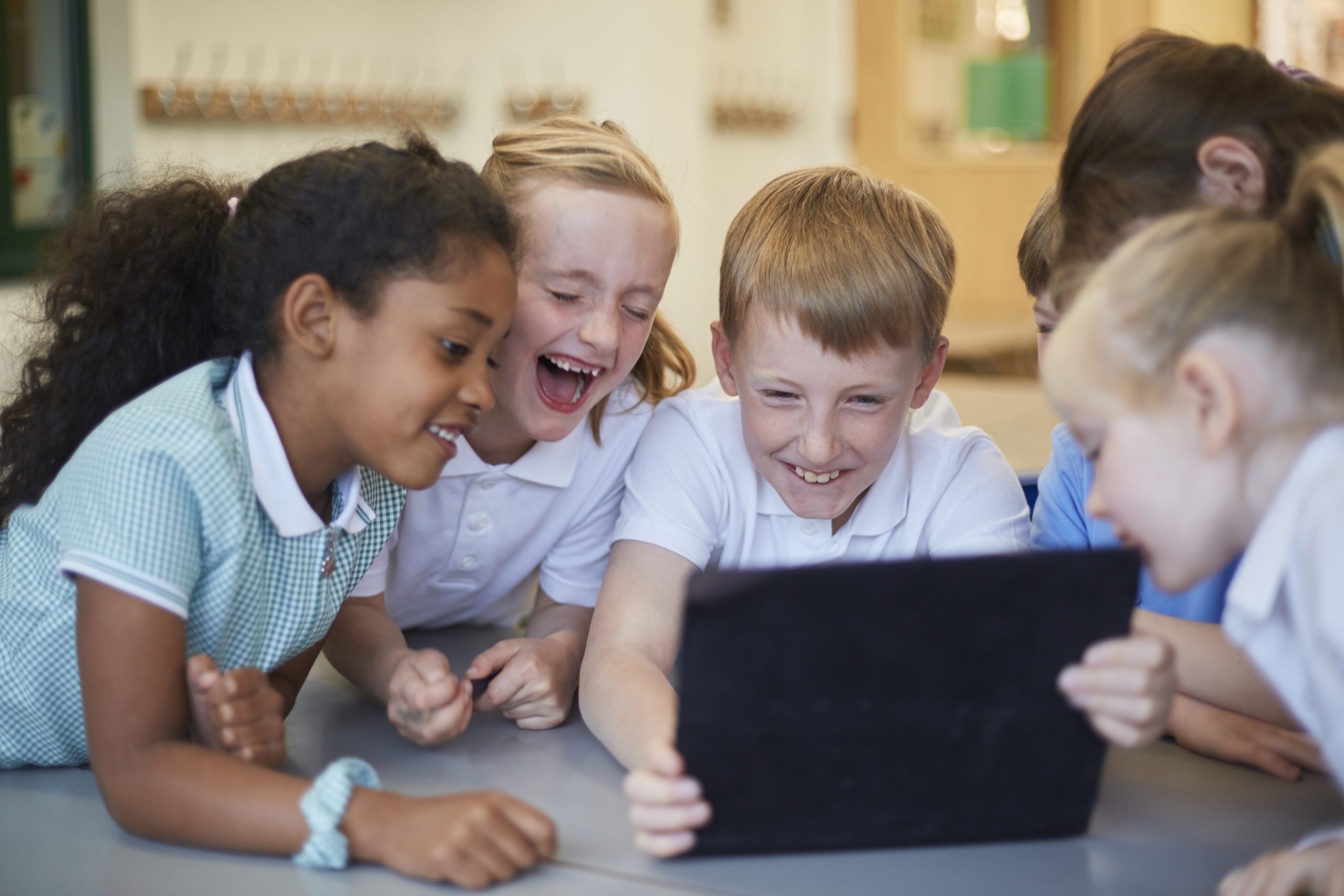 Schoolboys and girls laughing at digital tablet in classroom at primary school